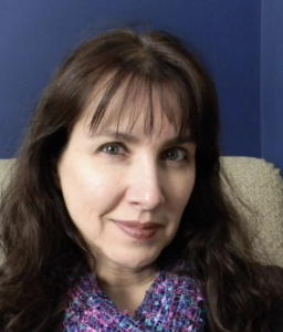 A headshot of a woman standing in front of a blue background.